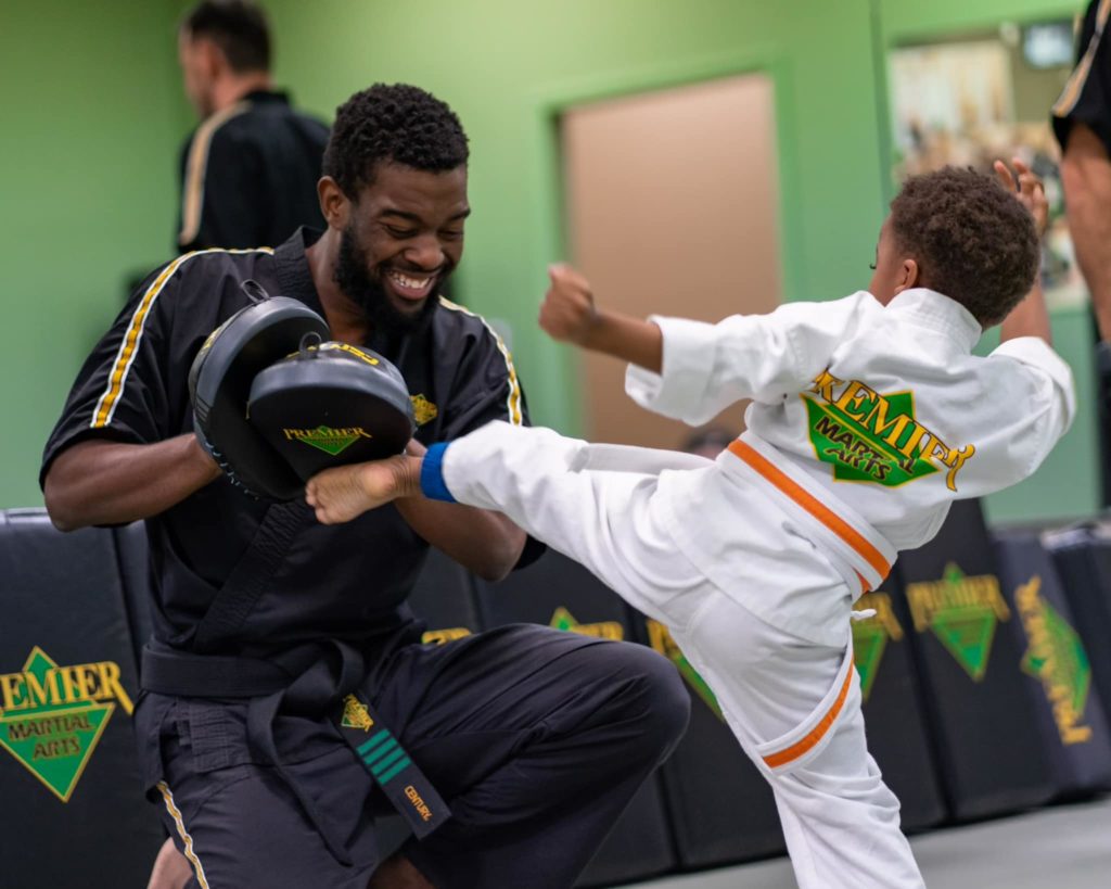 Young boy kicking a pad held by a coach in a martial arts class